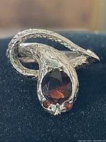 Close-up front view of the snake ring showing the large oval garnet stone on the head and two small round garnet eyes, with detailed scales on the coiled silver body.
