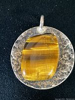Front view of vintage sterling silver pendant with polished tiger eye stone and textured silver background.