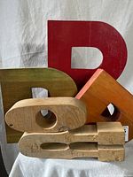 Group photo showing five vintage wood letters in various colors and sizes, stacked and leaning against each other.