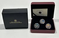 Closed black Royal Canadian Mint box with gold logo beside open burgundy display case with 3 coins and certificate inside.