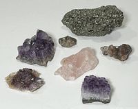 Overview photo showing all mineral specimens together including multiple amethyst clusters, a rose quartz stone, and pyrite clusters.