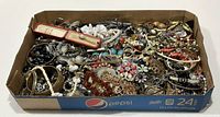 Wide shot of the full box filled with assorted jewelry pieces showing bracelets, brooches, necklaces, and rings.