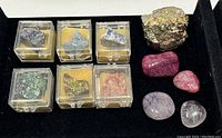 Top view of six mineral specimens in acrylic cases and five polished stones on black surface.