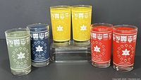Full set of 6 vintage Canadian Centennial drinking glasses in red, yellow, blue, and green colors, featuring provincial crests and maple leaf designs.