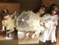 Three Ashton-Drake porcelain dolls displayed on a shelf with original packaging boxes behind them.