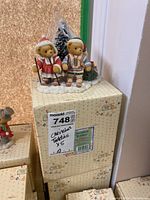 Photo showing Cherished Teddies Christmas-themed figurine pair atop original box with a pine tree backdrop.