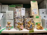 Shelf view of several Cherished Teddies figurines in front of original boxes with price tag 655 and labeled sizes 2.5 to 3.75 inches