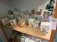 Wide view of multiple Cherished Teddies figurines displayed on shelves mostly with original boxes, showing quantity and variety of bears in different outfits and poses.