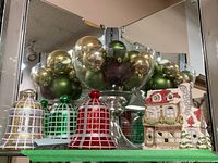 Overall photo showing the glass bowl filled with ornaments, ceramic house figurine, and three decorative glittery bells in white, green, and red with grid patterns.