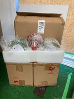 Three Christmas bell-shaped lamps wrapped in plastic, placed in foam padding inside a box.