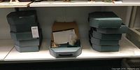 Shelf display of 11 green storage boxes for figurines, stacked in two piles, one box faded