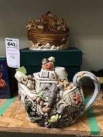 Front view of Noah's Ark figurine and teapot together on the shelf with the teapot in front and the Ark behind.