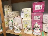 Group of Precious Moments figurines on shelf with original boxes stacked behind