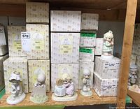 Shelf with multiple Precious Moments porcelain figurines arranged in front of their original boxes; various characters and poses visible.