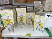 Multiple Precious Moments porcelain figurines displayed with original packaging in the background, including animal characters and labels with product names.