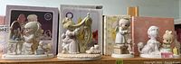 Four Precious Moments figurines displayed in front of their original boxes on a shelf.