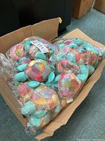 Box of multiple plastic-bagged plush turtles showing turquoise bodies and pastel multicolor shells.