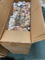 Top-down view of cardboard box filled with multiple sealed bags of Tender Tails plush