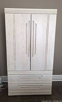 Front view of light wood armoire with closed doors and two drawers at bottom.