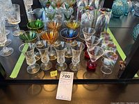 Wide view of multiple barware pieces including colored stemmed glasses and clear glasses with rainbow bases.