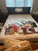 Full view of the wood veneer bed with mattress and various books on the mattress. Bed headboard has inset oval mirror and shelves.