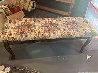 Full side view of the bench showing wood veneer frame with curved legs and floral upholstered cushioned top.