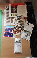 Top view of various Canadian stamp blocks and loose sheets on a desk, showing multiple themes including Queen Elizabeth and sports.