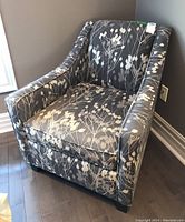 Front angled view of the pewter fabric armchair with floral branch pattern showing fabric condition and shape.