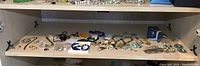 Wide shot of shelf holding multiple pieces of assorted costume jewelry including earrings and necklaces arranged loosely