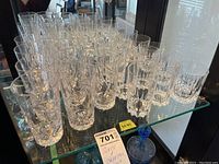 Multiple clear crystal and glass drinking glasses displayed on a mirrored shelf, showing intricate pinwheel and faceted cut patterns