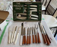Boxed Crown Sheffield 'The Miracle Edge' knife set with white-handled knives and spare blades, laid out with other cutlery sets on table.