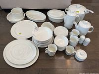 Overview of white ironstone dishes, cups, and serving pieces laid out on floor.