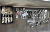 Flatware arranged on floor showing approximately 100 pieces including forks, spoons, knives, and serving utensils with a small boxed gold plated set on the left.