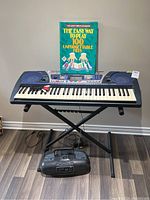 Yamaha PSR-262 keyboard on stand with songbook on music rest and Radio Shack boombox on floor beneath keyboard.