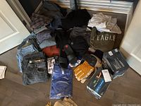 Overview of lot including jeans, shirts, hats, gloves, and footwear scattered on the floor.