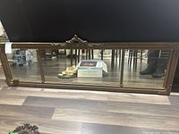 Full view of the long rectangular mirror on floor showing the overall wood and brass frame, reflections, and wear on frame edges.