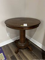 Full view of the table showing round top, pedestal base, and carved lower detailing.