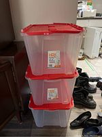 Three stacked clear HDX plastic totes with red flip top lids in room with assorted items