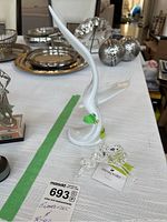 Photo of white ceramic bird figurine with chip on beak and two Swarovski crystal bird figurines on table with other silver and decorative items visible in background.