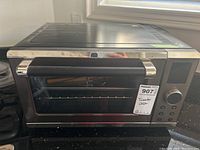 Front view of the Paderno toaster oven showing glass door, handle, and control buttons.