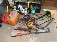 Overview of various tools, gardening supplies, booster cables, and jerry cans on garage floor