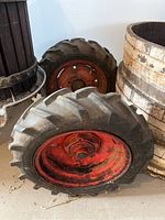 Photo showing two used tractor tires with red rims leaning against wooden barrels indoors.