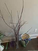 Overall view of the vases arranged on floor including the tall clear glass bud vase with dogwood filler, ceramic floral vase, and two square glass vases.