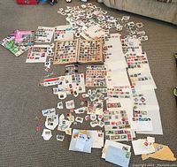 Overview of the large assortment of stamps spread out on floor, includes loose stamps, albums, and various sheets composed of stamps from various countries.
