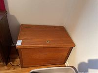 Front and angled view of the vintage wooden flip-top chest showing the warm brown wood finish and brass pull handle on the flip-top lid.