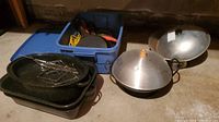 Overview photo showing stacked cast iron pans, metal roasting rack, aluminum wok, and blue plastic storage bin with cords and other miscellaneous items.