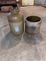 Two vintage stoneware crocks of different sizes on the floor showing overall shape and color