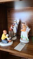 Three porcelain figurines from Doulton's Childhood Days collection, showing children with animals on a wooden shelf.