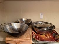 Two stainless steel mixing bowls, stainless steel pan with lid, two wooden cutting boards stacked, and floral print tray below.