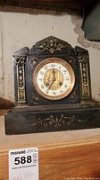 Full view of the black marble or stone mantel clock showing its architectural style with decorative gold accents and a central clock face.